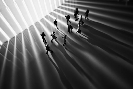 Miniature toys studio set up - Top view of black and white effect of people with long shadows busy walking during sunrise or sunset. Noise added for dramatic effect.