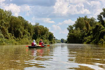 Fototapeta na wymiar Couple - man and woman paddling in a canoe in a wild beautiful Danube river and lake on biosphere reserve in spring. Summer kayaking