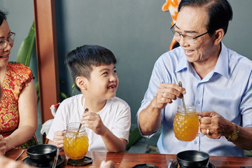 Cute little boy resting in cafe with grandparents and drinking sweet delicious cocktails