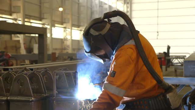 Steel worker with oxygen mask welding on steel installation in factory hall- camera dolly movement - direction left