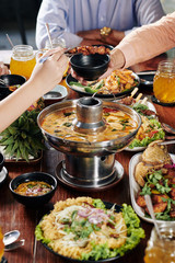 Hands of people eating delicious Asian food like squid soup, fish, fried shrimps and skewers at...
