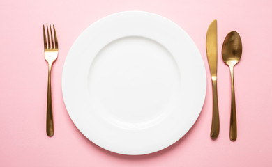 Gold cutlery and dishes set against pink background, formal place setting