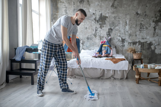 Smiling bearded man mopping the floor at the weekend