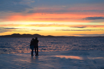 Incredible sunset (sunrise, dawn) at sea with silhouettes of people (couple) in Zadar (Croatia)