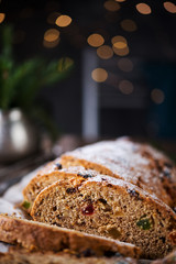 A traditional German Christmas Stollen lies on a wooden table. A celebratory cake is cut into slices with candied fruits, nuts and raisins. Selective focus.