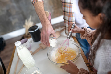 Father adding flour while daughter whipping eggs for pie
