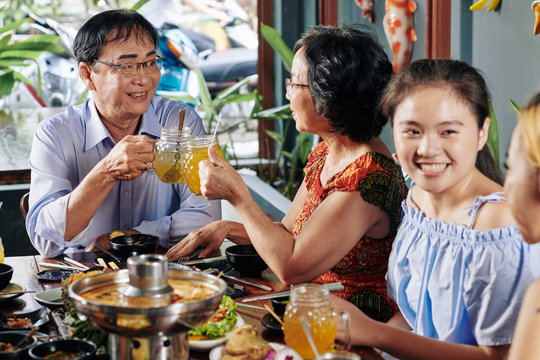 Cheerful senior couple toasting with glass mugs when having dinner with theis children and grandchildren