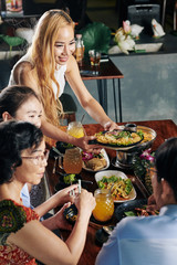 Beautiful smiling Vietnamese woman serving tasty dish she made for family dinner