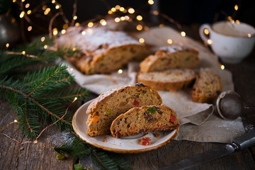 A traditional German Christmas Stollen lies on a wooden table. A celebratory cake is cut into slices with candied fruits, nuts and raisins. Selective focus.