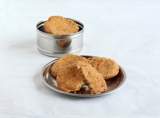 Mathri, a delicious, Indian home cooked vegetarian food, with a golden-brown crust and flaky inner layers, is eaten as a side dish or snack, on a steel plate.
