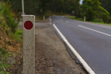 Light reflector in red color on white post at side of road