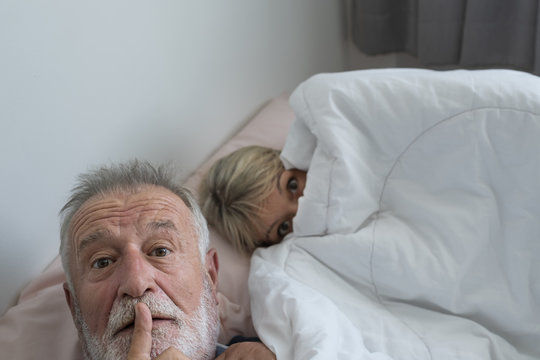 happy elderly couple caucasian senior man selfie with woman resting together in white blanket in bedroom, retirement love lifestyle concept