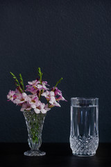 A glass of water and purple flowers in a vase placed on the table