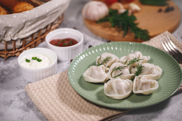 Ravioli on a plate with dill, served with sauce and ketchup. Boiled dumplings on a dish. Tasty dinner. Food. Close-up.