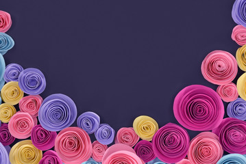 Pink, yellow and purple rose flat lay background with crafted paper flowers at bottom and empty dark  copy space in middle