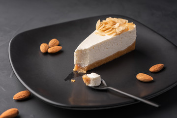 Cheesecake on a black plate among almonds , cut a slice in a spoon.