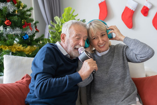 senior elderly old man and woman happy to sing song and listening with headphone together in living room that decorated with christmas tree, retirement lovely lifestyle concept