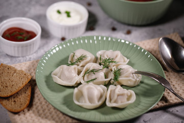 Ravioli on a plate with dill, served with sauce and ketchup. Boiled dumplings on a dish. Tasty dinner. Food. Close-up.