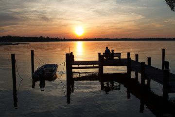 The sun sets over a bay of water as a silhouetted fishing boat dock occupies the foreground at dusk