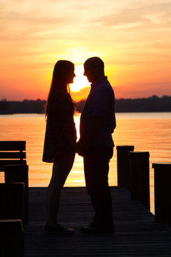The silhouette of a male and female straight heterosexual couple getting romantically closer together on a dock at sunset