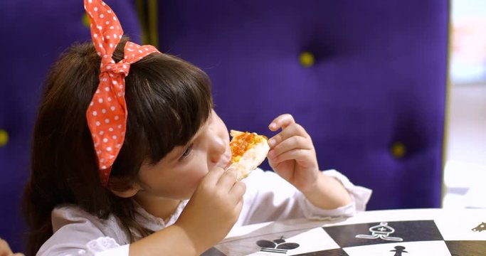 Children eat pizza. Two cute girls of four and seven years old are sitting at a table in a pizzeria  holding slices of pizza and eating. Slow motion 50 FPS 4k. Close up portrait