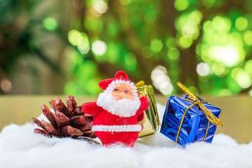 Little santa claus with pine cone and group of giftbox on white cotton with green boken bacjground. Christmas concept.