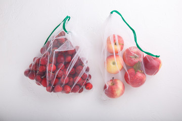 Apples in textile grocery mesh bags. Red fruits and vegetables in reusable eco friendly packaging on white background.