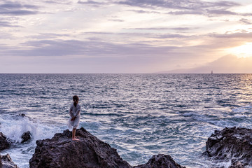 A little girl in a beautiful white dress standing on a rock in front of the ocean watching sunset, Maui , Hawaii