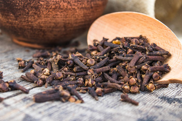 A spice of dried cloves lies on a wooden spoon and is scattered on old wooden boards.