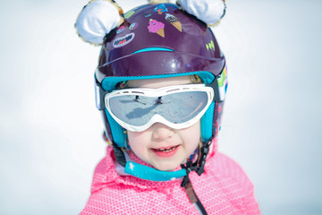 Portrait of cute happy skier girl in helmet and goggles in a winter ski resort
