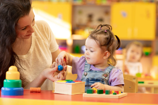 Woman and child girl talking and smiling while playing with educational toys together in daycare centre