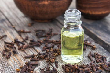 Clove oil in a glass bottle on old wooden boards near dry clove spices.