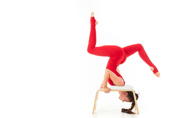 Caucasian gymnast with athletic body stands on her head, does warm-up and stretch muscles