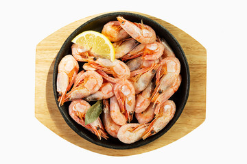 Prawns with lemon in a portioned cast-iron frying pan on a wooden board. Isolated over white background.