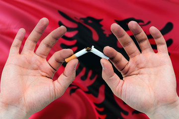 Albania quit smoking cigarettes concept. Adult man hands breaking cigarette. National health theme and country flag background.