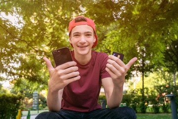 Teenage boy with a credit card and phone makes purchasing outdoors. Happy young man is using smart phone and bank card for online shopping. Handsome smiling white guy holds bank  card and cell phone.
