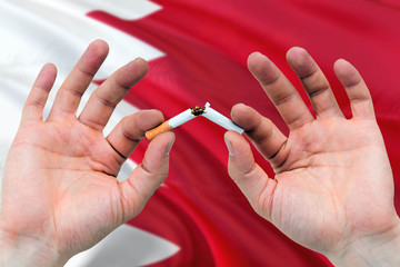 Bahrain quit smoking cigarettes concept. Adult man hands breaking cigarette. National health theme and country flag background.