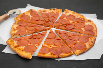 Tasty Pepperoni pizza on parchment over black background, side view. Close-up.