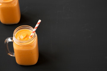 Homemade pumpkin smoothie in glass jars over black surface, low angle view. Copy space.