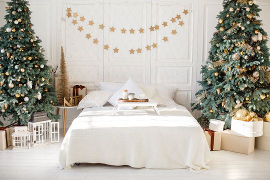 Romantic bedroom in light colors with a lot of garland lights decorated for New Year Celebrating. Christmas mood at home. White bedroom and Christmas spruces. Romantic interior. Breakfast in a bed