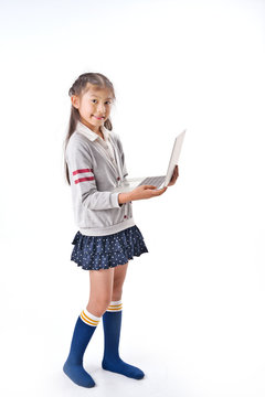 Portrait of a smiling asian little girl holding laptop computer while standing and looking at camera isolated over white background