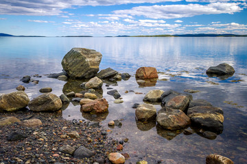 Stones on the shore of the Kandalaksha Bay of the White Sea. Clouds and sky reflected in water