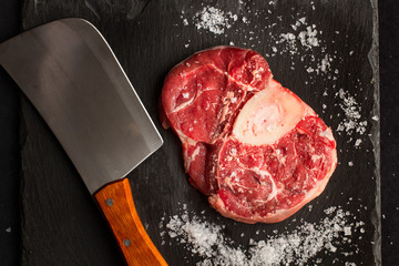 Osobuco carne cruda vista desde arriba sobre pizarra negra con hacha de cocina cuchillo