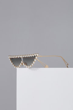 Subject Shot Of Cat Eyes Sunglasses With Rhinestone Rim, Gray Lenses And Golden Temples. The Sunglasses Are Isolated On The White Square On The Gray Background. 