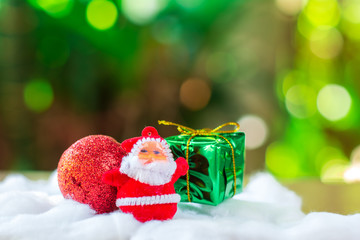 Little santa claus with red ball and group of giftbox on white cotton with green boken bacjground. Christmas concept.