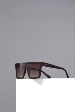 Subject Shot Of Square Oversized Sunglasses With Thick Brown Frame And Brown Lenses. The Sunglasses Are Isolated On The White Square On The Gray Background. 