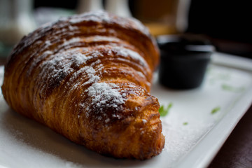 croissant in powdered sugar on a white plate. apricot jam in a black little plate next to a croissant