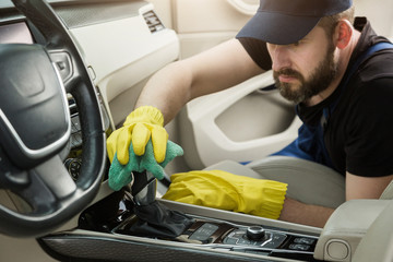 Cleaning service. Man in uniform and yellow gloves washes a car interior in a car wash