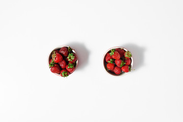 Two bowls with ripe strawberries on a white surface. Top view.