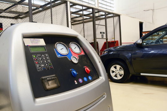 the car's air conditioning service tool with functional button on the black panel standing at the ground at car service shop with the black car